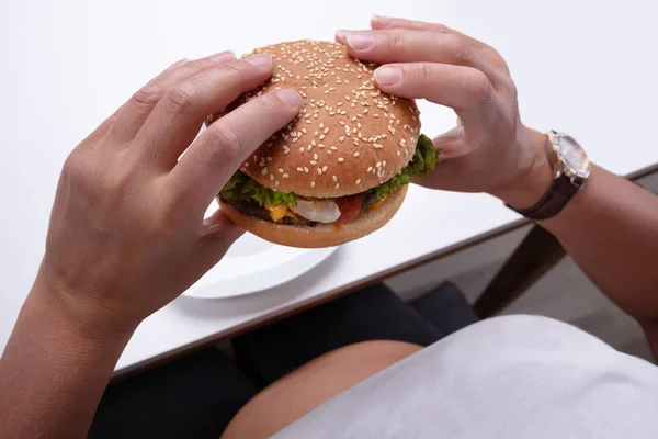 ハンバーガーを手に持った太りすぎの女性の頭上図 — ストック写真