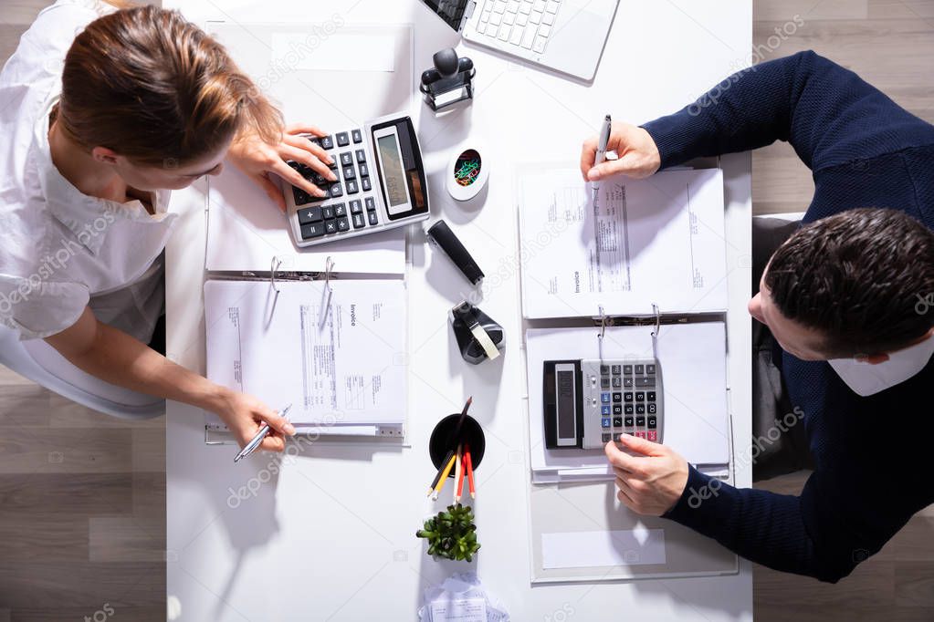 High Angle View Of Male And Female Businesspeople Calculating Invoice With Calculator In Office