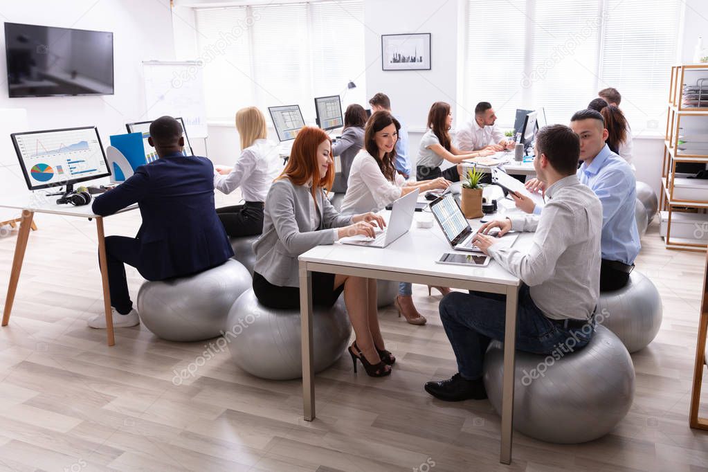 Group Of Multi-ethnic Businesspeople Sitting On Fitness Ball Having Discussing While Working In Office