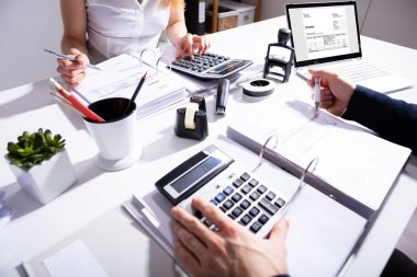 Elevated View Of Two Businesspeople Calculating Invoice With Calculator At Workplace clipart