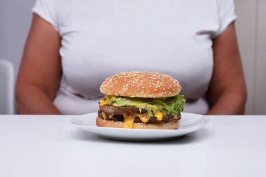 Kilolu kadın önünde masanın üzerinde beyaz çanak üzerinde Fast Food Hamburger