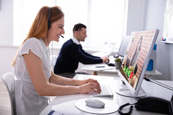 オフィスのコンピュータで彼女の同僚とビデオ会議中にヘッドセットを身に着けている笑顔のビジネスウーマン — ストック写真