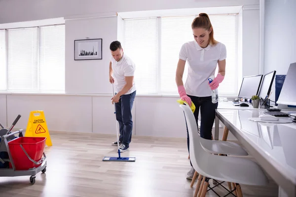 Två Leende Young Vaktmästaren Rengöring Skriv Bord Och Mopping Golv — Stockfoto