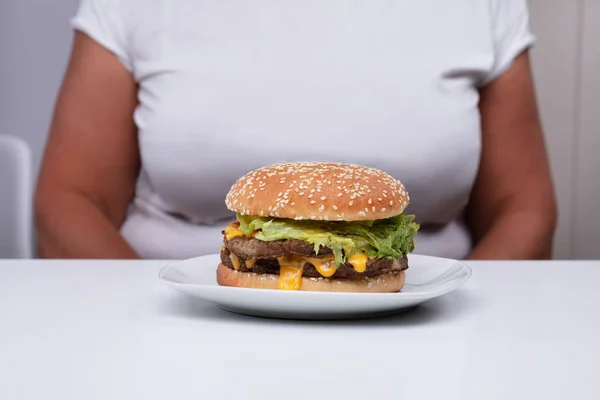 太りすぎの女性の前でテーブルの上に白い皿の上にファーストフードハンバーガー — ストック写真