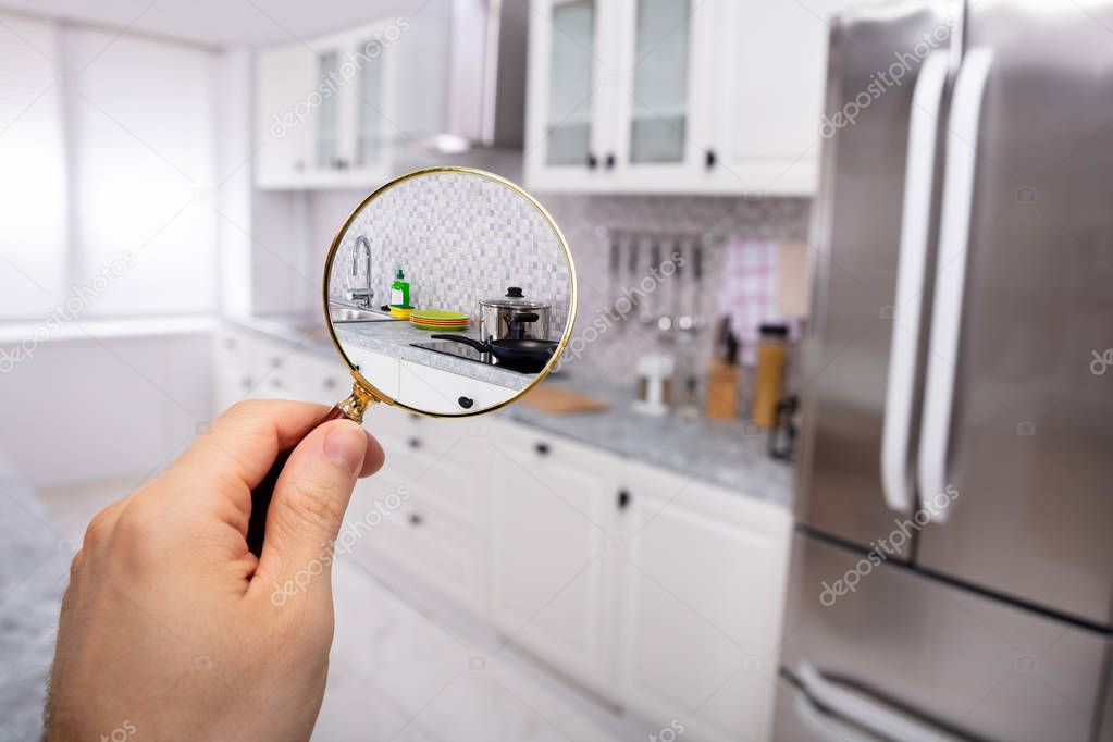 Close-up Of A Man's Hand Holding Magnifying Glass Over The Kitchen In Modular Kitchen