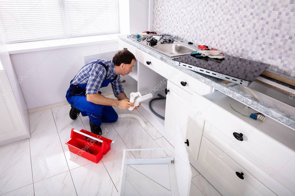 An Overhead View Of Male Plumber Installing Sink Siphon In Domestic Kitchen