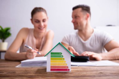 Ahşap Masa Üzerinde Hesap Makinesi kullanarak Mutlu Çift Önünde Enerji Verimliliği Oranı Gösteren Ev
