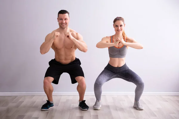 穿着运动服的快乐健身情侣在健身房做蹲式练习的侧视图 — 图库照片