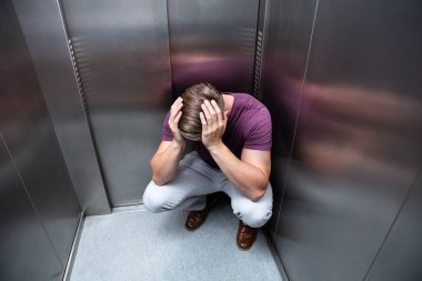 Crouched Worried Man With Hands On Head In Elevator clipart