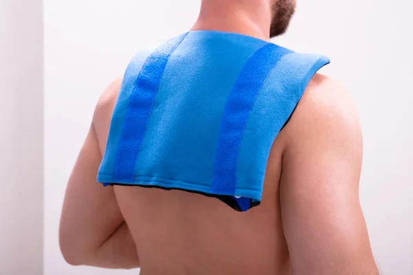 肩と背中に青いアイスパックを持つシャツのない男の背面図 — ストック写真