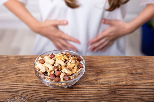 Bowl Of Nuts On Table In Front Of Woman Suffering From Stomach Pain