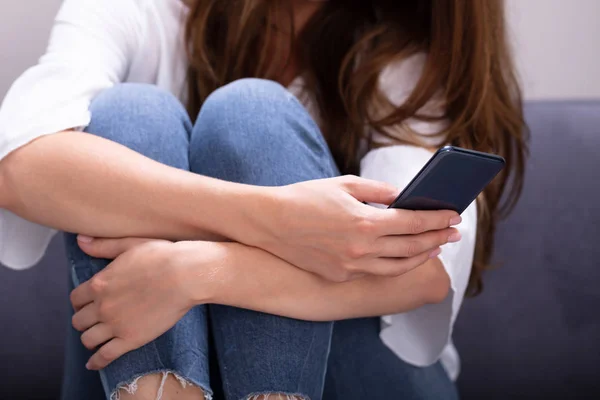 スマートフォンでソファのテキストメッセージに座っている女性のクローズアップ — ストック写真
