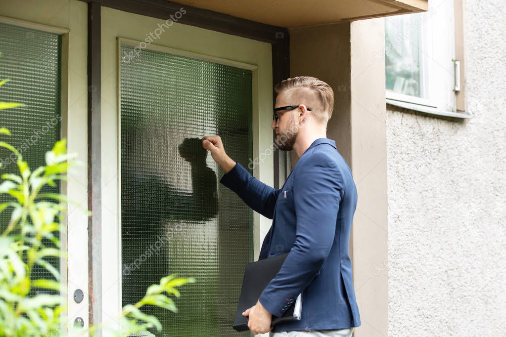 Man Standing At The Entrance Of The House Knocking The Door