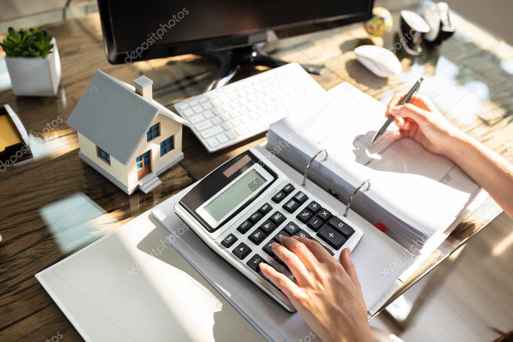 An Elevated View Of A Real Estate Agent Calculating Tax Over Wooden Table