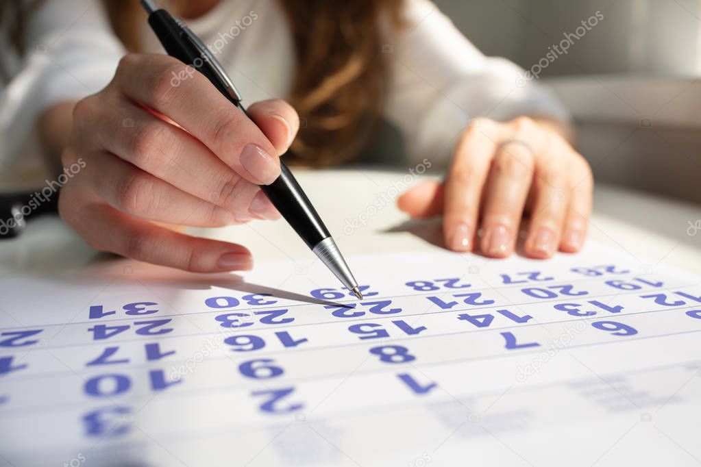 Close-up Of A Businesswoman's Hand Marking With Pen On Calendar At Workplace