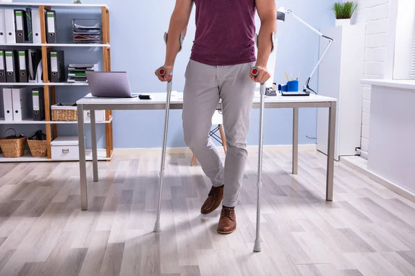 職場で松葉杖を持つハードウッドフロアを歩く障害者ビジネスマン — ストック写真