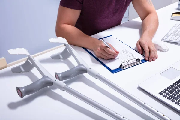Behinderte Männliche Patientin Füllt Versicherungsantrag Mit Krücken Über Schreibtisch Aus — Stockfoto