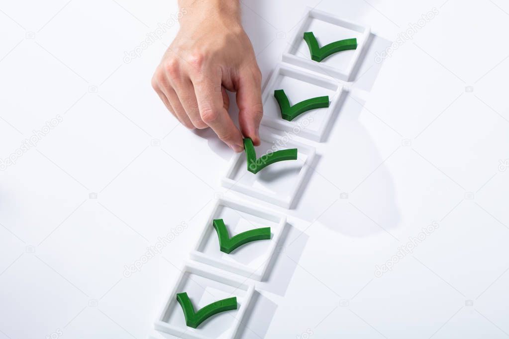 High Angle View Of Man's Hand Placing Green Check Mark In Box Over White Backdrop