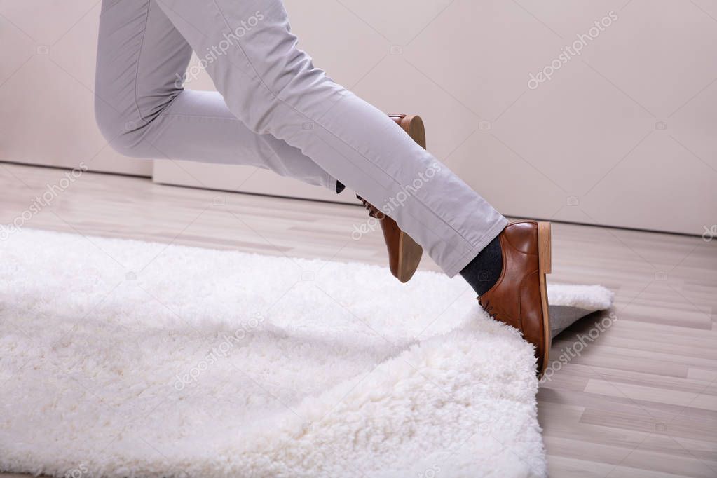 Low Section Of Man Legs Stumbling With A Carpet At Home