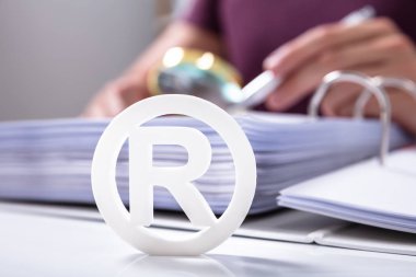 Close-up Of White Registered Trademark Sign Near Documents Over Desk clipart