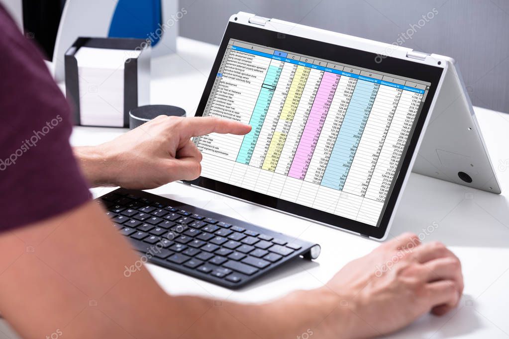 Close-up Of A Businessman's Hand Examining Spreadsheet On Laptop In Office