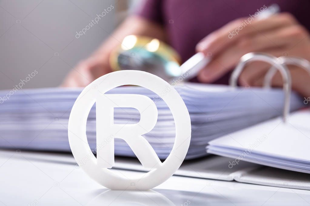 Close-up Of White Registered Trademark Sign Near Documents Over Desk