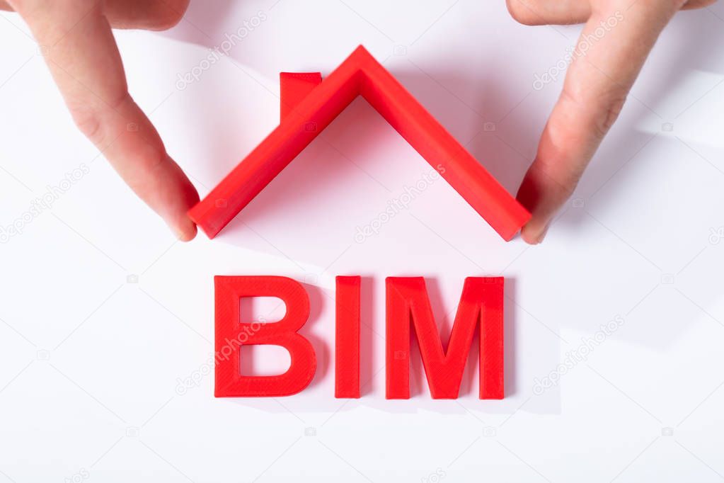 Elevated View Of Human Fingers Holding Roof With BIM Text Over White Desk