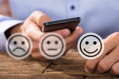 Ahşap Masa Üzerinde Cep Telefonu Kullanan Adamın Önünde İfadeleri Gösteren Simgeler