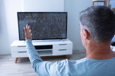 Televizyonun karşısında oturan ve sinyal almayan bir adam.