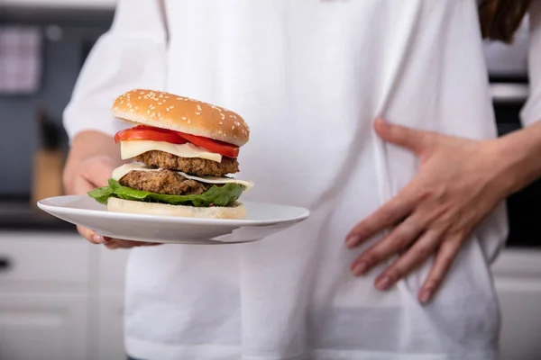 ハンバーガーを食べながら胃痛に苦しむ女性の中間部 — ストック写真