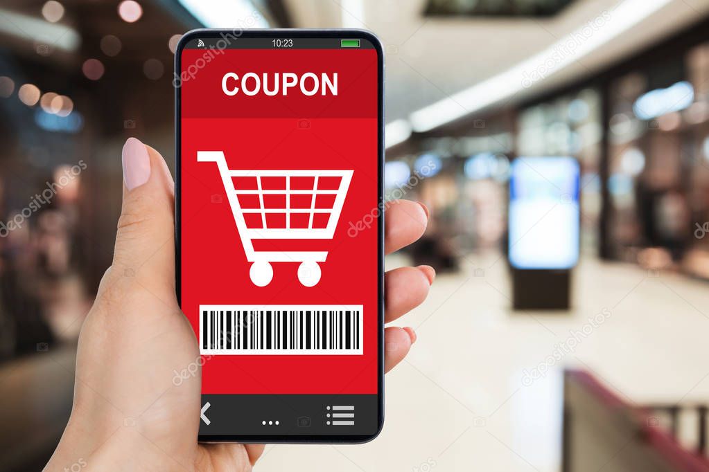 Close-up Of Woman's Hand Holding Smartphone With Shopping Coupon In Mall