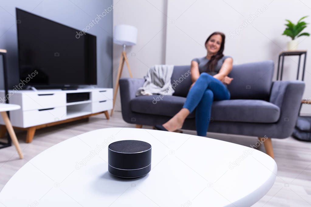 Close-up Of Wireless Speaker In Front Of Woman Sitting On Sofa