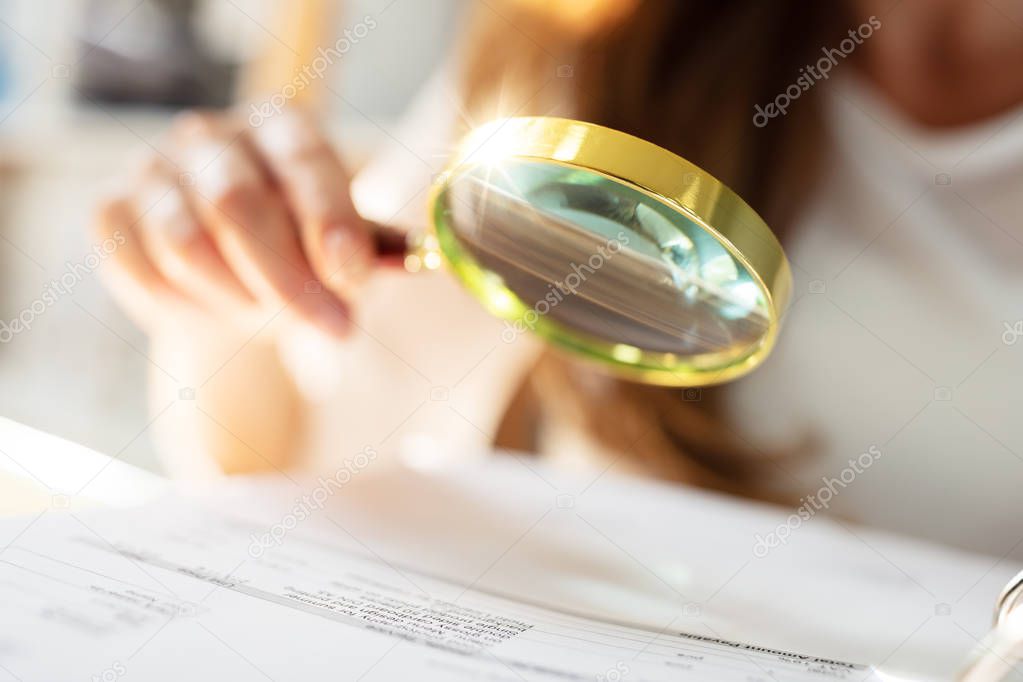 Businessperson Analyzing Bill Through Magnifying Glass In Office