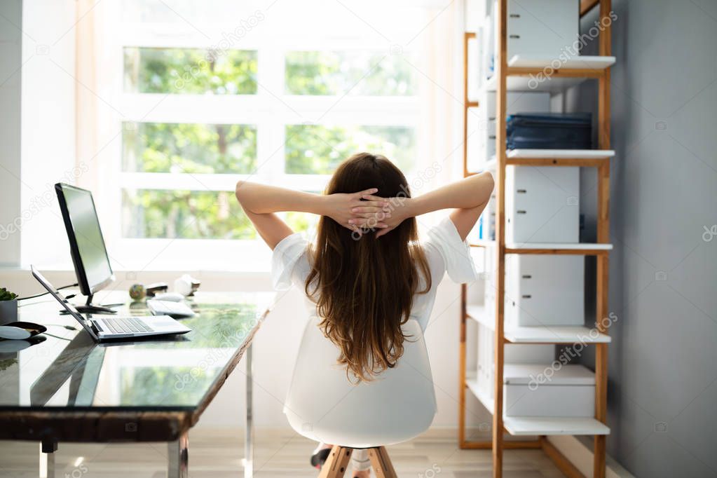 Rear View Of Relaxed Businesswoman With Hands Behind Head Sitting In Office