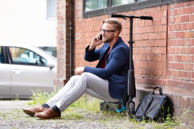 Yakışıklı İşadamı Tuğla duvara yakın Cep Telefonu Kullanarak Elektrikli Scooter Üzerinde Oturan