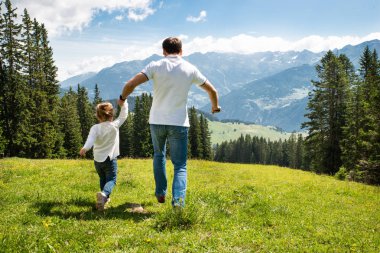 Baba ve kızı dağlarda tarlada koşarak el ele tutuşuyor