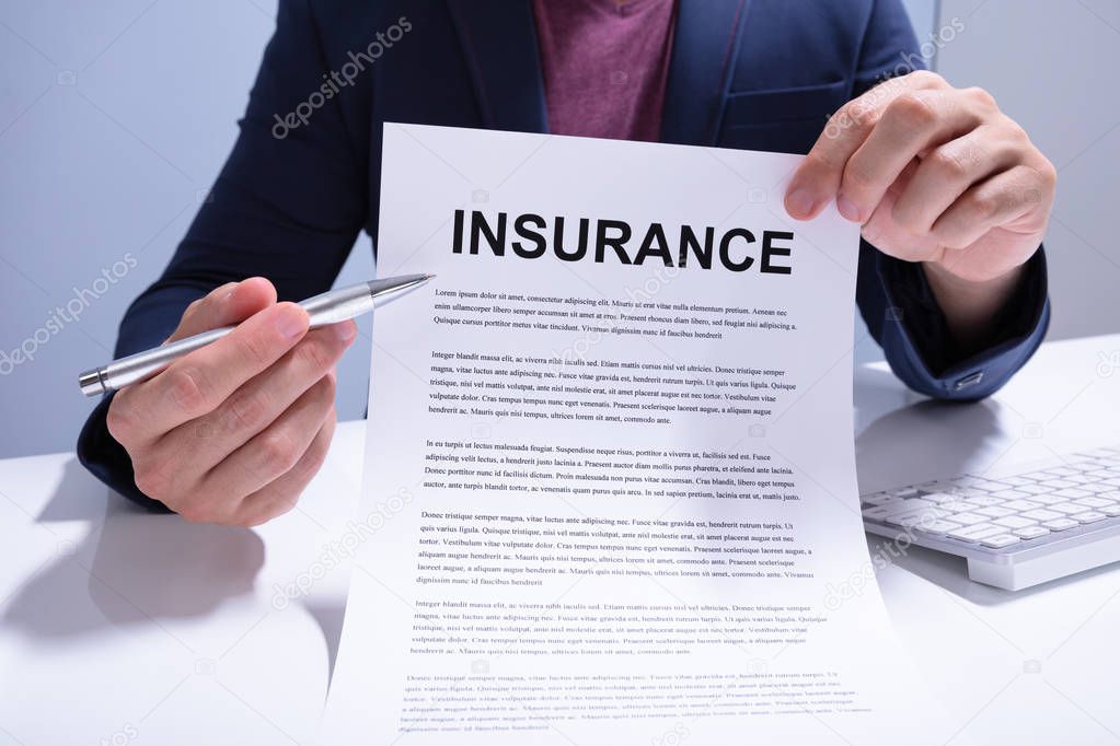 Mid Section Of A Businessman Showing Insurance Document Over White Desk At Office