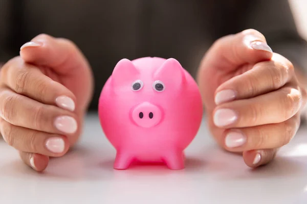 白い机の上のピンクの貯金を保護する人間の手のクローズ アップ — ストック写真