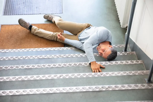一个成熟的人在滑倒和摔倒事故后躺在楼梯上 — 图库照片