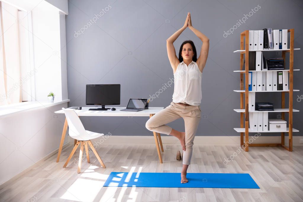 Young Businesswoman Doing Yoga At Workplace In Office