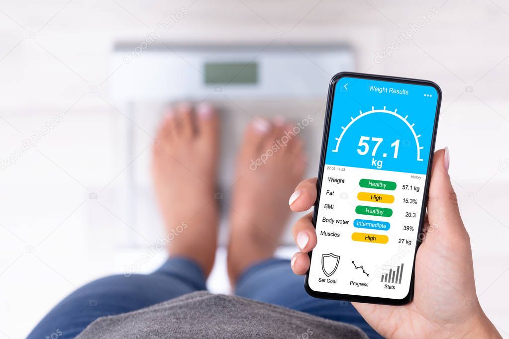 High Angle View Of A Woman Standing On Weighing Scale Holding Cellphone