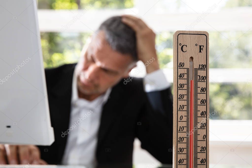 Thermometer In Front Of Businessman Working During Hot Weather In The Office