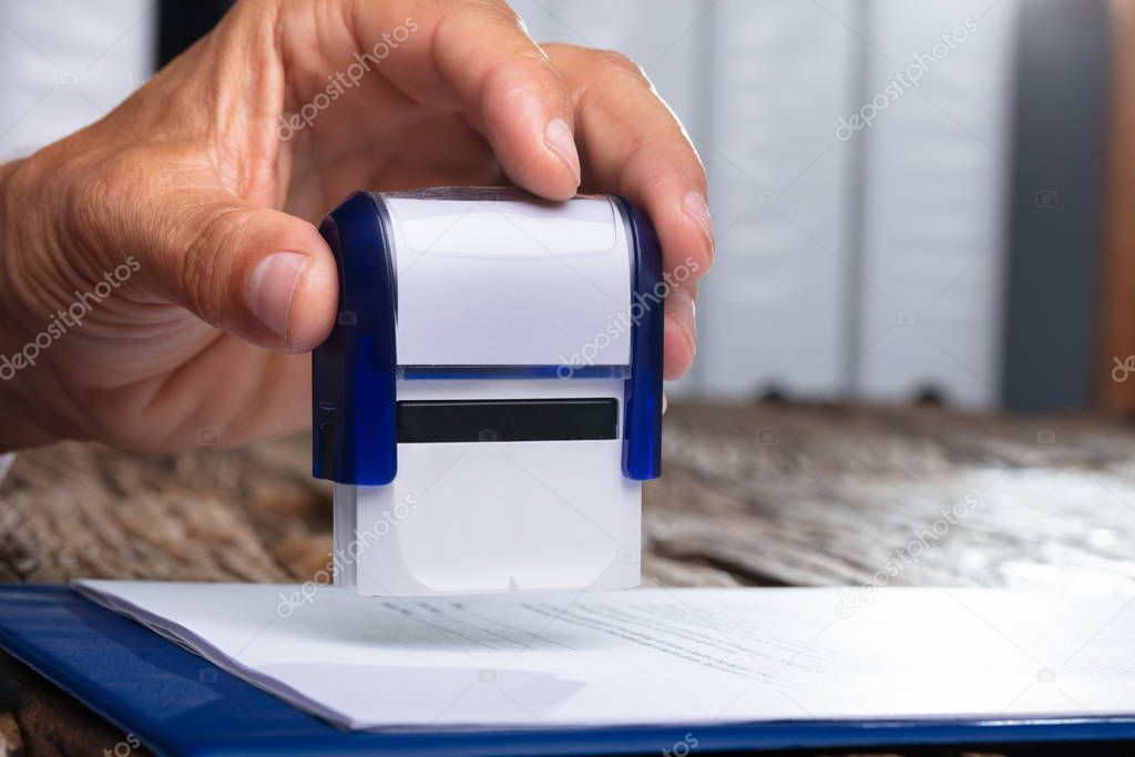 Close-up Of Person Hands Pressing Stamper On Document