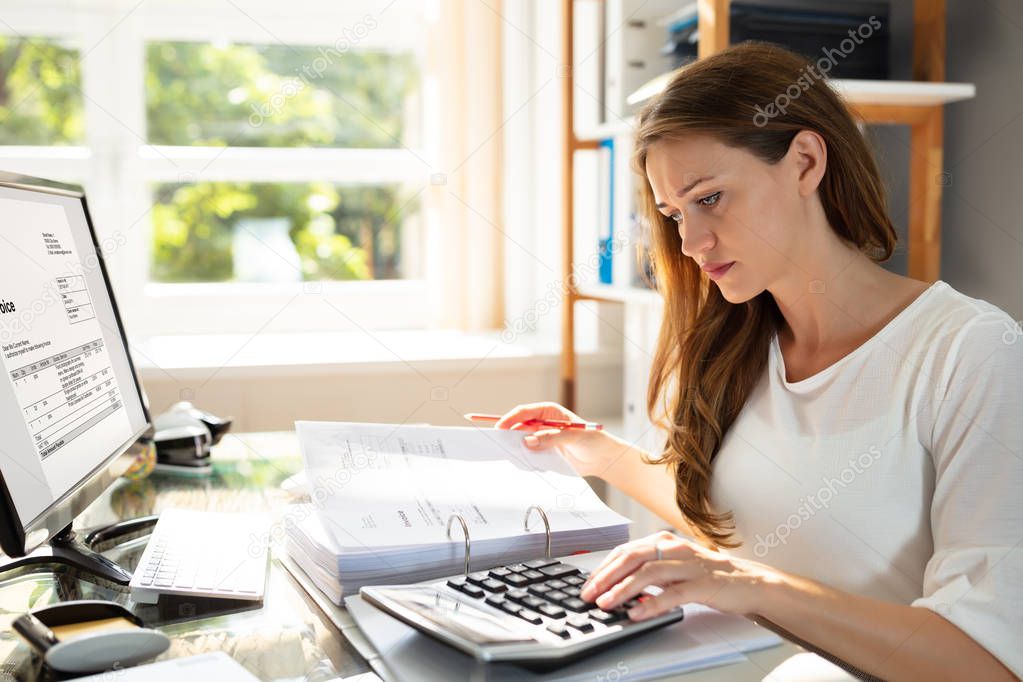 Close-up Of A Businesswoman's Hand Calculating Invoice In Office