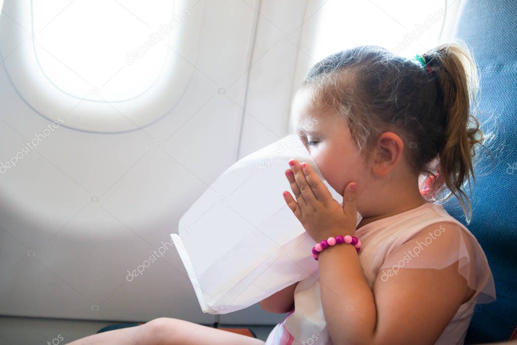 Side View Of Little Girl Is Vomiting In The Airplane Using A Sickness Bag
