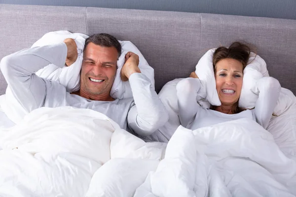 ベッドの上に枕で耳を覆う騒音によって邪魔された成熟したカップル — ストック写真
