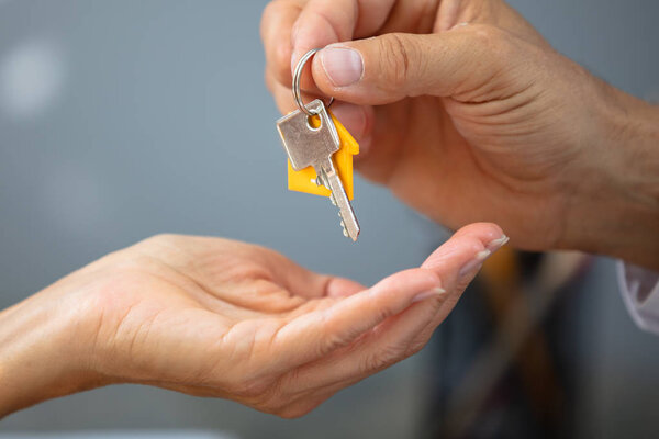 Close-up Of An Estate Agent's Hand Giving House Key To Woman