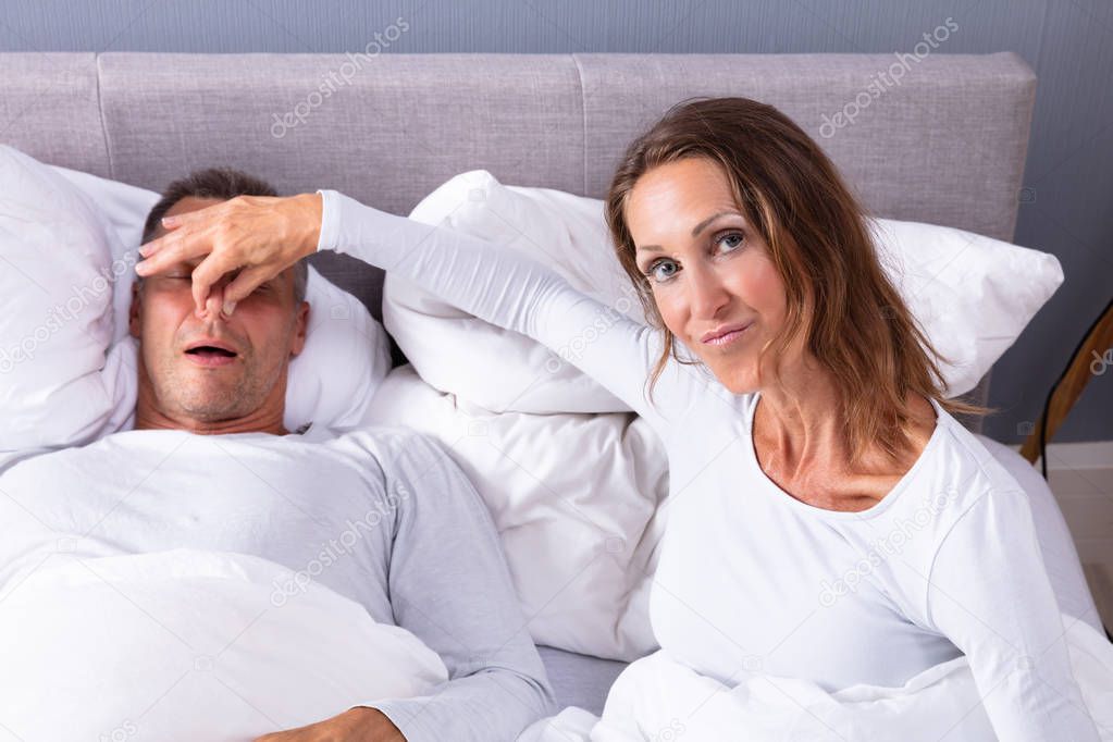 Disturbed Mature Woman Holding Her Husband's Nose To Stop Him From Snoring On Bed