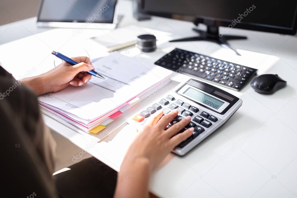 Young Businesswoman Calculating Invoice With Calculator At Desk
