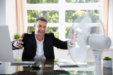 Businessman Sitting Near Fan In Office During Hot Weather clipart